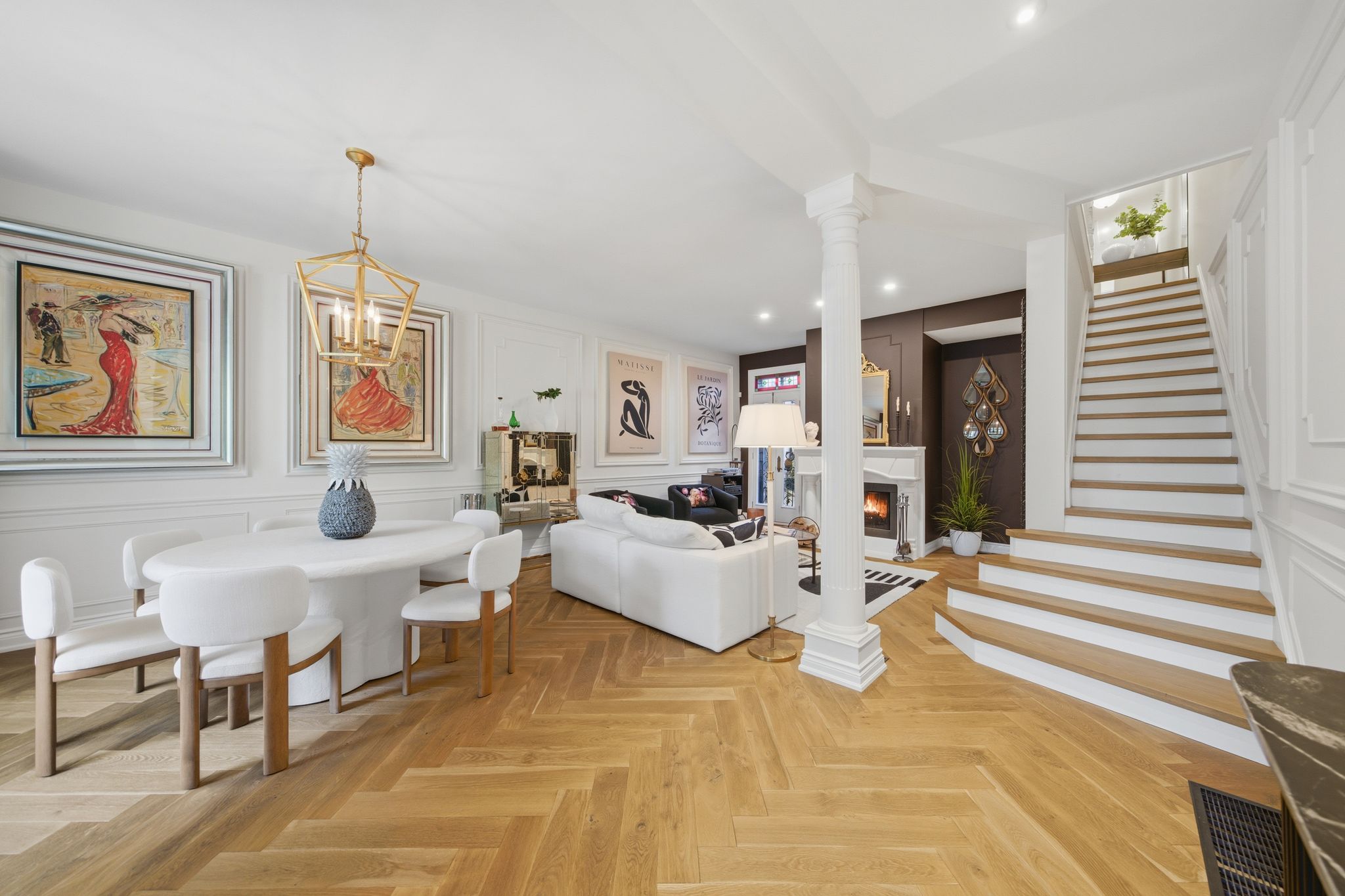 Open living and dining room with wood staircase, white fireplace, and herringbone hardwood floors