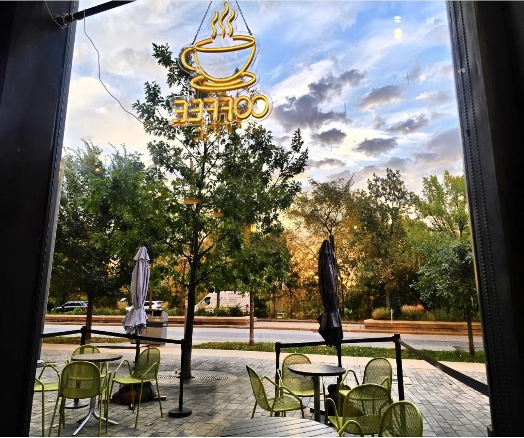 The view from the front-row seats at Birds & Beans Caf&eacute; — neon coffee sign over the patio at golden hour