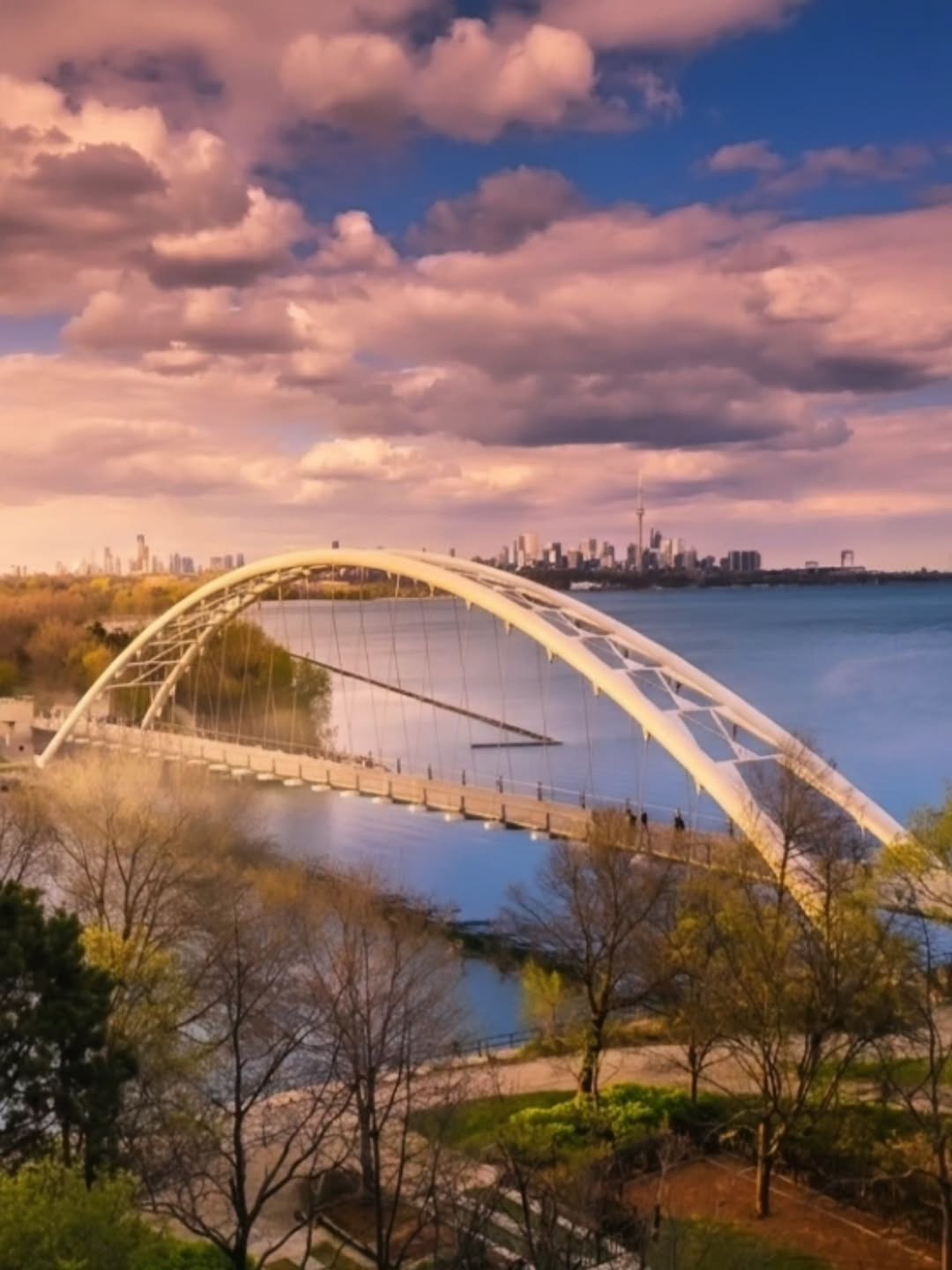 The Humber Bay Arch Bridge spanning the water at golden hour, Toronto skyline behind, seen from Palace Place
