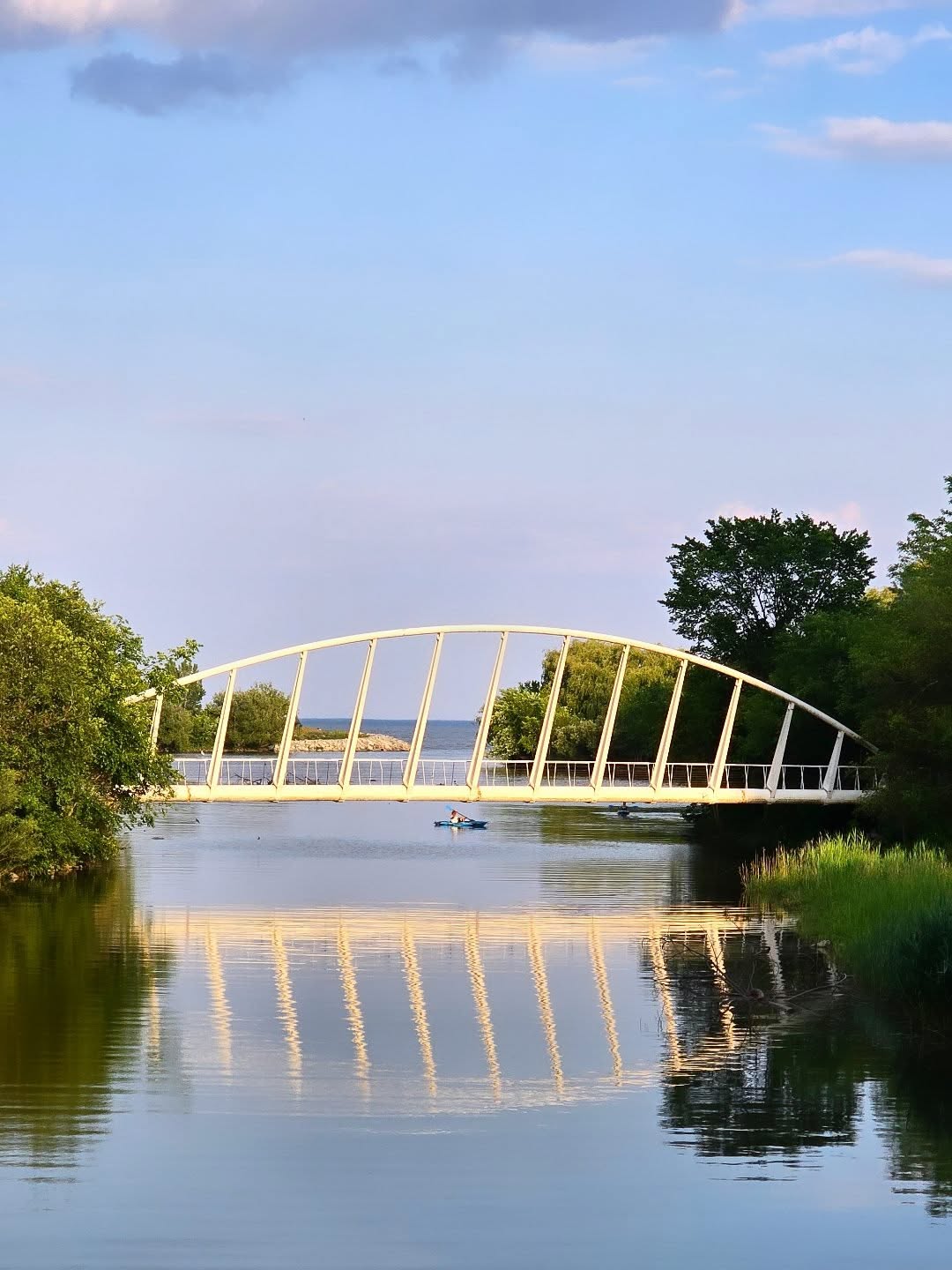 The Humber Bay Arch Bridge mirrored in the water with a kayaker passing beneath