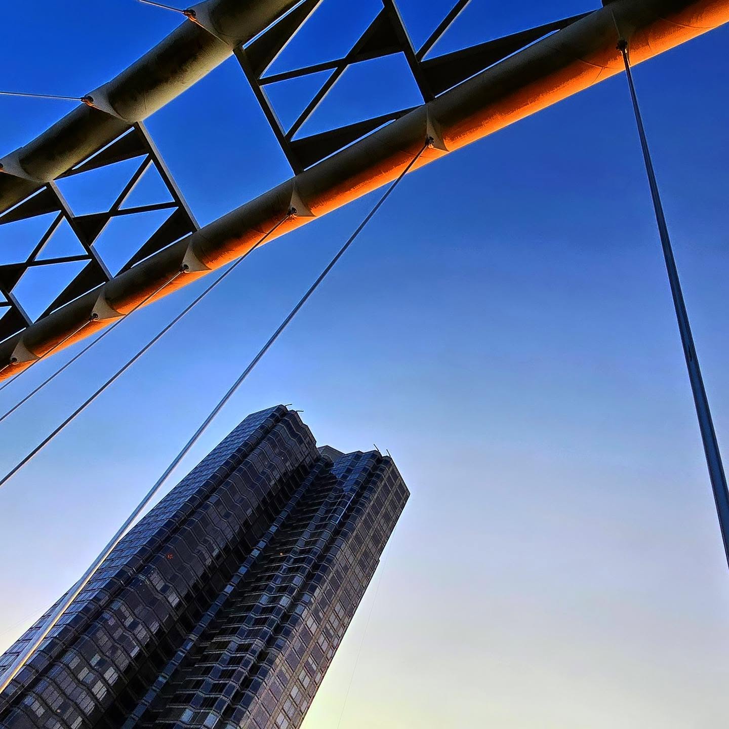Looking up at the Humber Bay Arch Bridge truss glowing at sunset with the Palace Place condo tower below