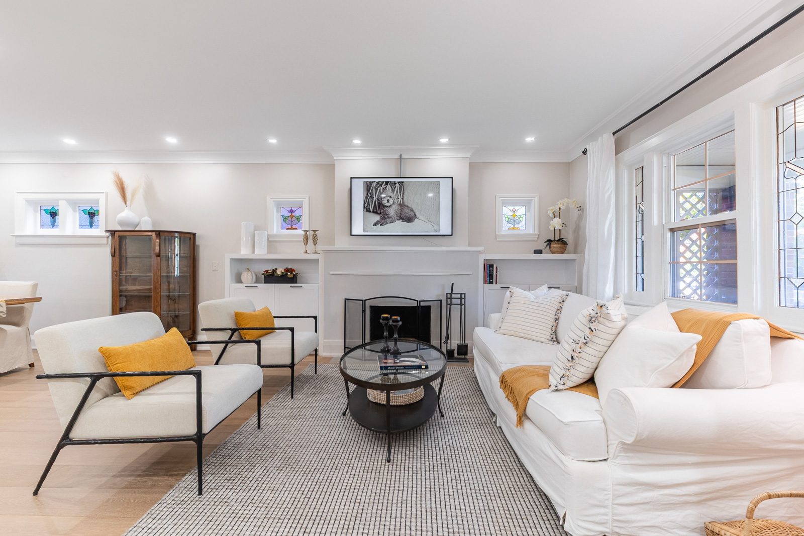 Staged living room with a white sofa, mustard cushions and stained glass windows at 171 Melrose Avenue, Toronto