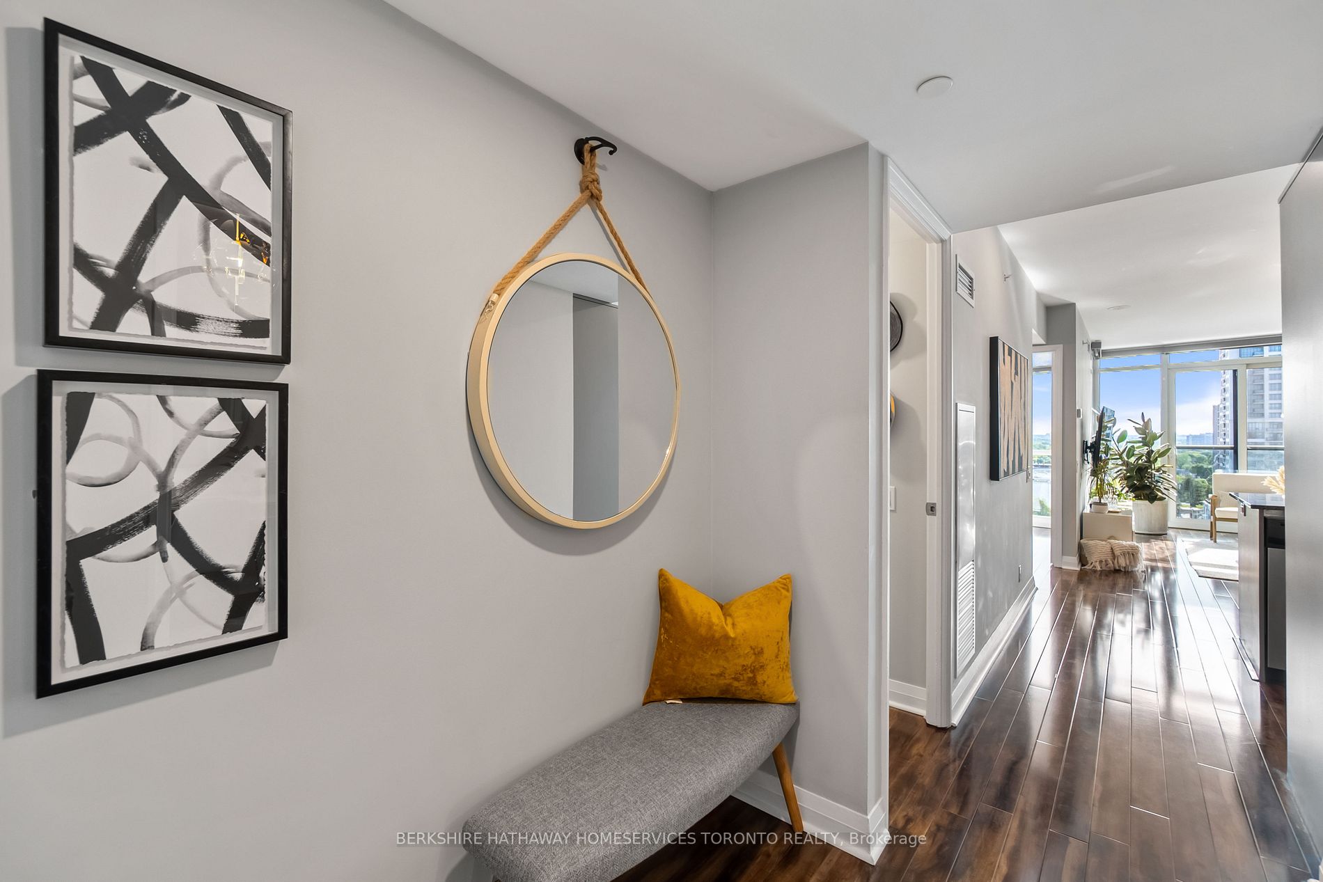 Entry foyer with round rope-hung mirror, bench and abstract art, leading into the suite