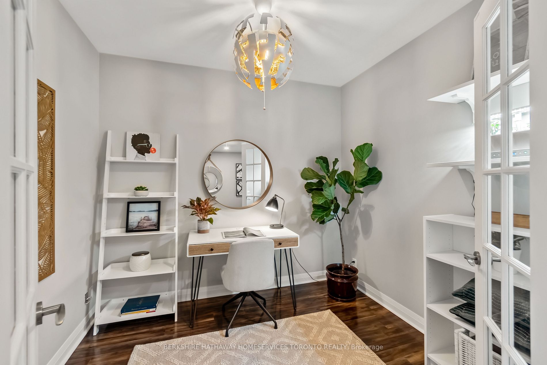 The den styled as a home office, with desk, ladder shelf, round mirror and french doors