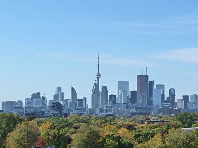 The Toronto skyline with the CN Tower rising over autumn trees &mdash; the southwest view from Unit 914 at The Carlaw, 1190 Dundas Street East