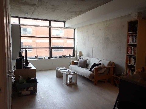 Open living and dining room at Unit 306 with large windows, exposed concrete ceiling, and hardwood floors