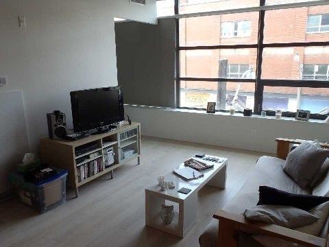 Living room at Unit 306 with large windows overlooking the street, TV and media stand