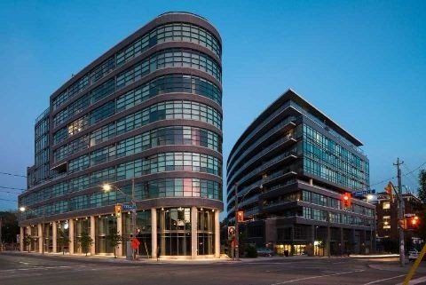 The iconic Flatiron Lofts at 1201 Dundas Street East, Toronto at dusk &mdash; the curved glass and brick soft-loft building at Dundas and Carlaw