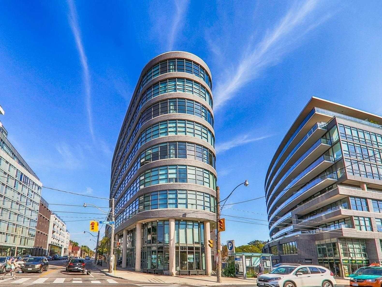 The iconic Flatiron Lofts at 1201 Dundas Street East, Toronto &mdash; a curved glass and brick soft-loft building at Dundas and Carlaw