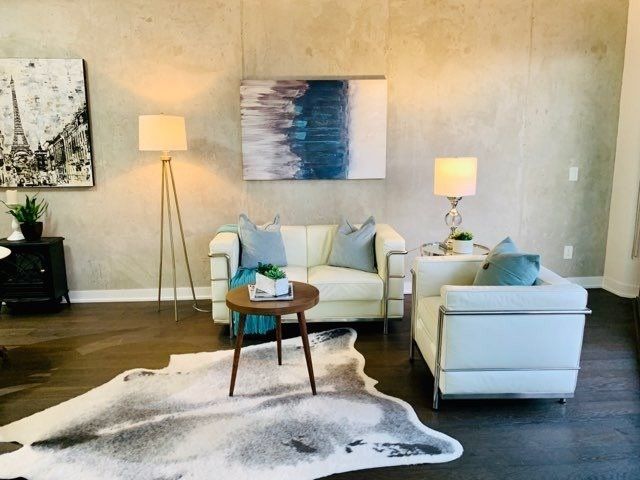 Staged living room at Unit 901 with white sofas, exposed concrete wall, and contemporary art