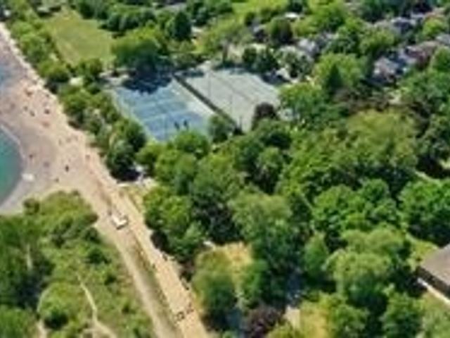 Aerial view over the Beaches neighbourhood toward Lake Ontario, with tennis courts, mature trees and the beach
