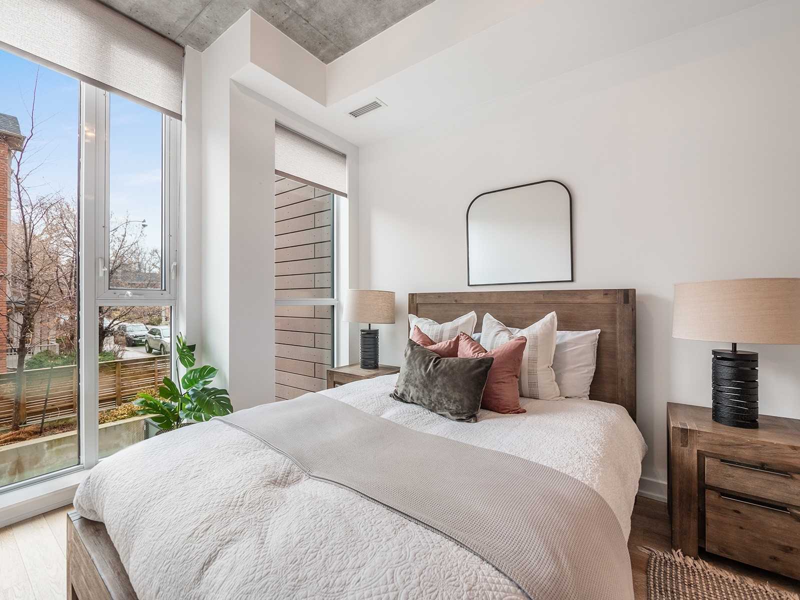 Primary bedroom with king bed, wood nightstands, and large windows overlooking the tree-lined enclave