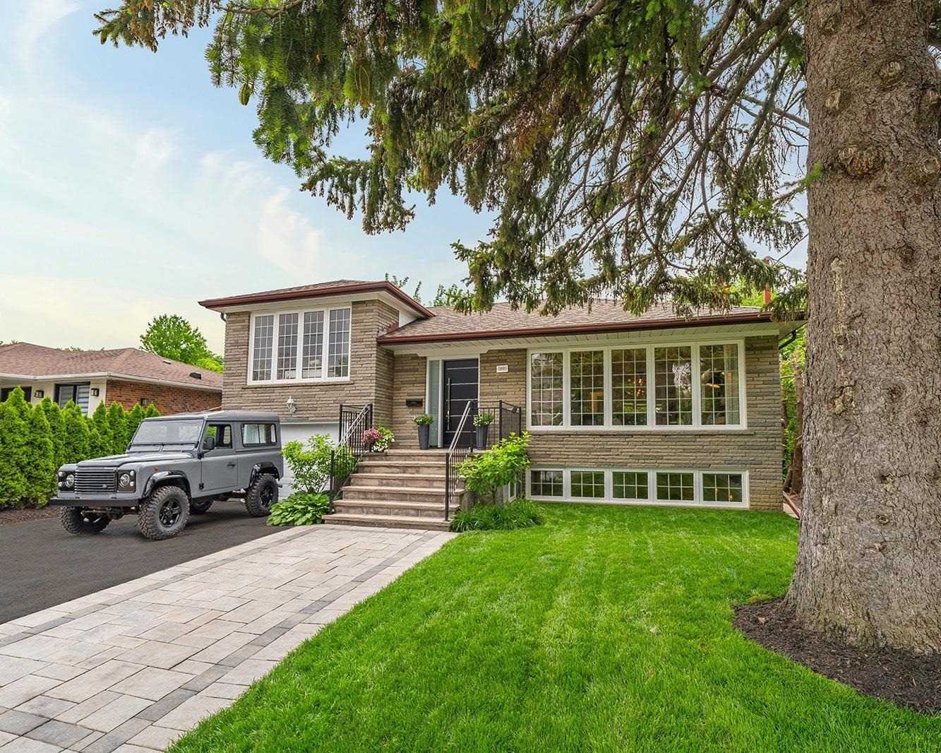 Front exterior of 177 Clanton Park Road, a brick raised bungalow with mature pine trees and a stone walkway