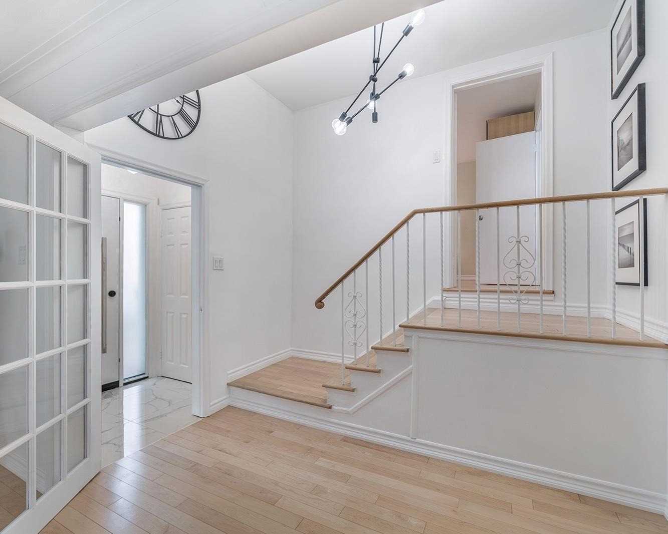 Bright entry foyer with staircase, modern chandelier, and large wall clock