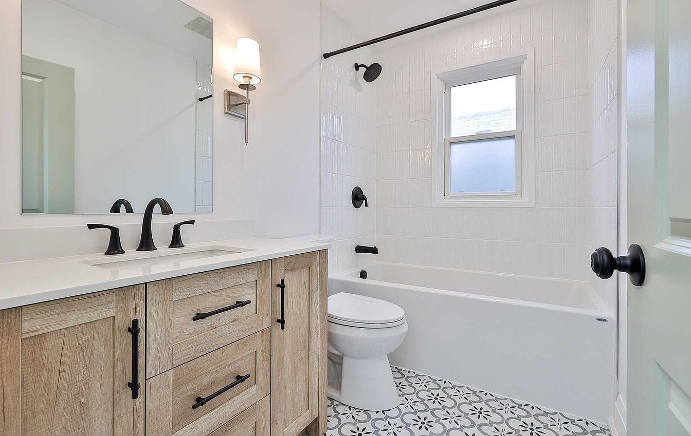 Renovated bathroom with wood vanity, black fixtures and patterned floor tile