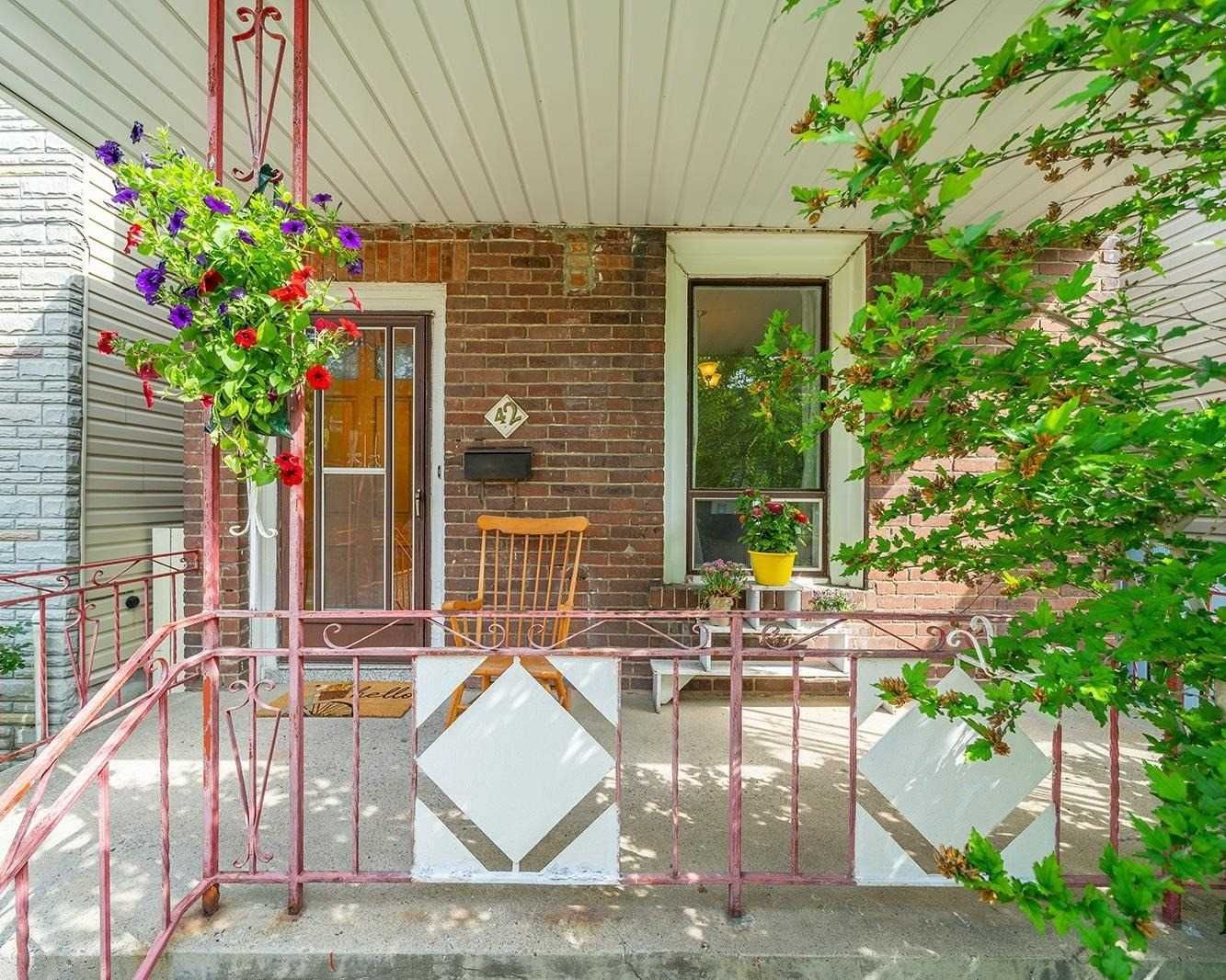Covered front porch of 42 Melville Avenue with the number 42 plaque, rocking chair, and hanging flower baskets