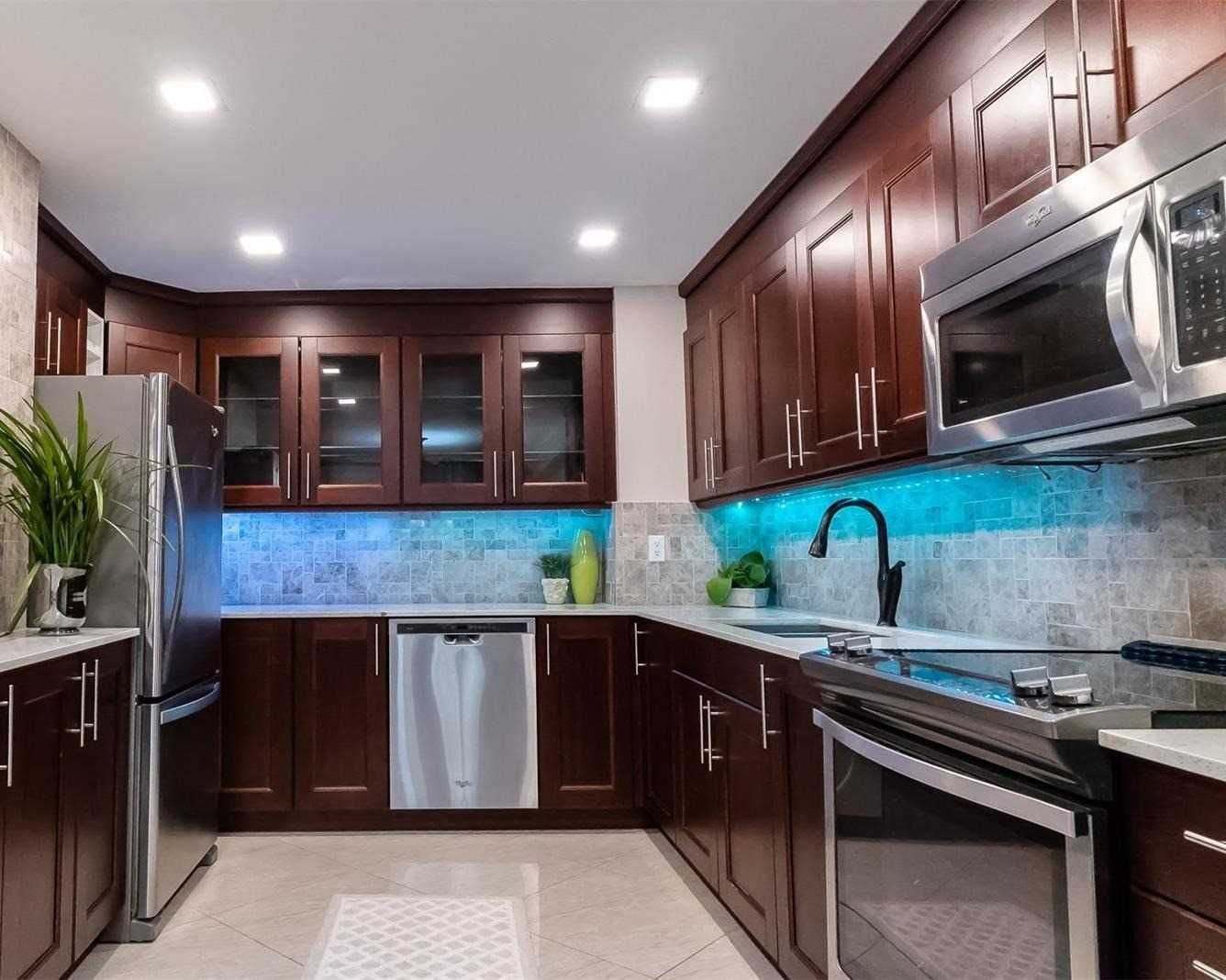 Kitchen with stainless steel fridge and dishwasher, glass-front cabinets and under-cabinet lighting