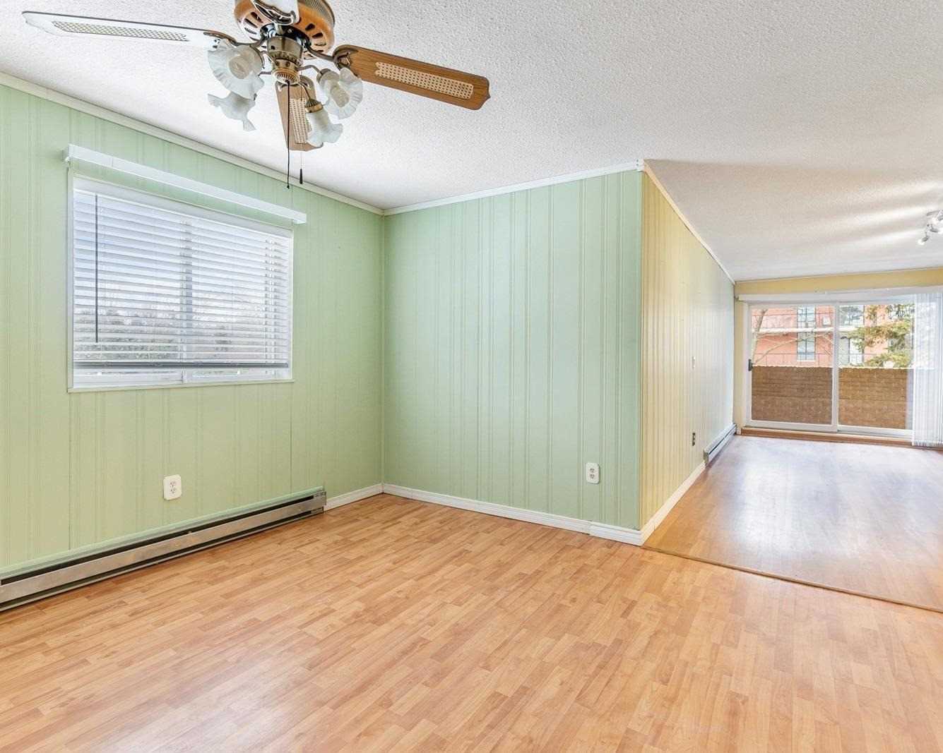 Bright living room with green accent wall, ceiling fan, and sliding doors to the enclosed balcony